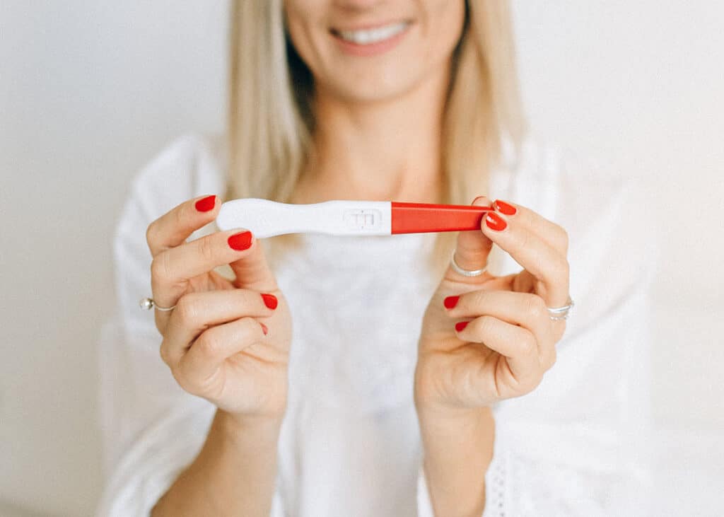 woman with red nails holding positive pregnancy test
