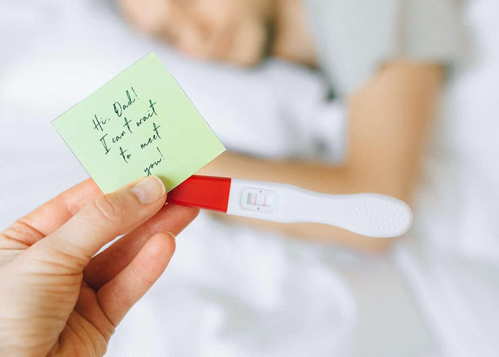 woman holding pregnancy test with note to dad